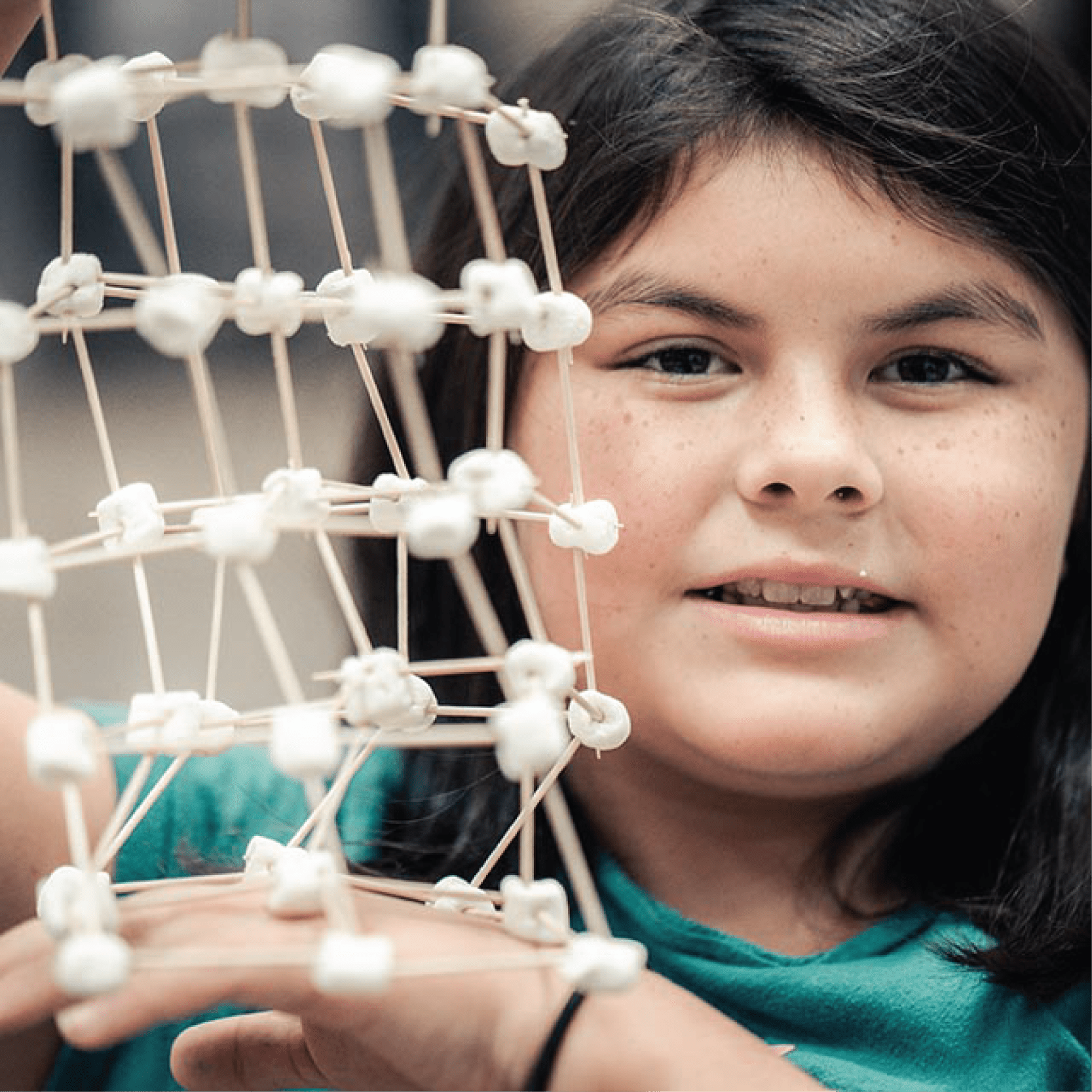 A girl proudly holds up her rectangular STEM creation made up of toothpicks and mini-marshmallows.