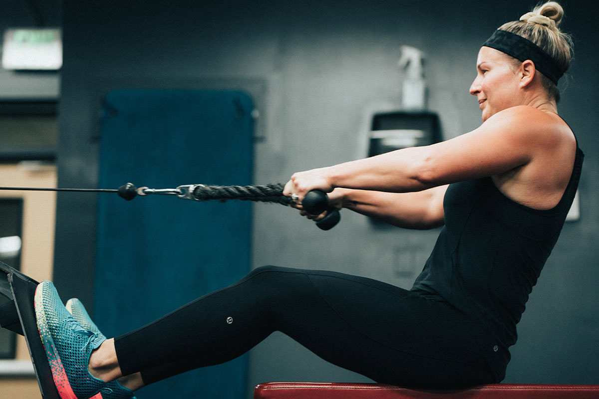 A woman uses a rowing machine. She is wearing all black exercise clothes and a black sweat headband.