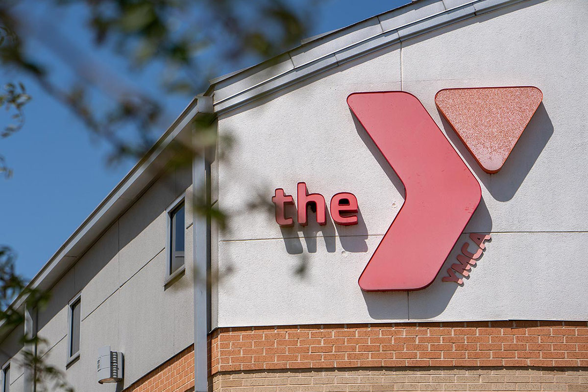 The top half of a building and its curved roofline are viewed through the soft focus of tree branches. A YMCA logo is on the building.