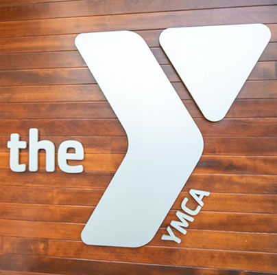 A metal YMCA logo is mounted on a warm wooden wall.