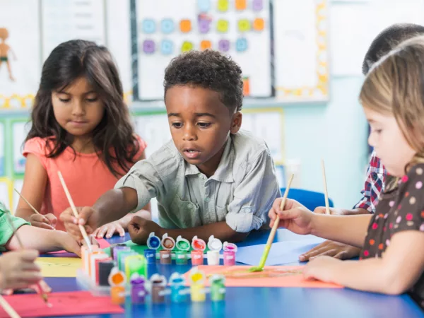 Children sit at a table with many colorful arts and crafts.