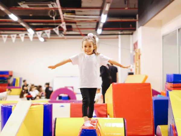 A girl stands atop a tumbling cushion in a gymnastics arena.