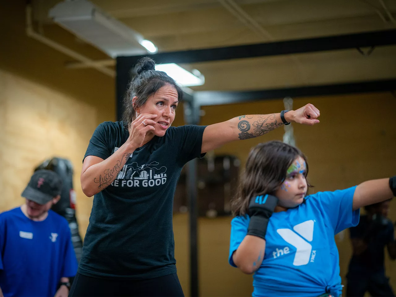 A woman demonstrates a boxing pose to a child.