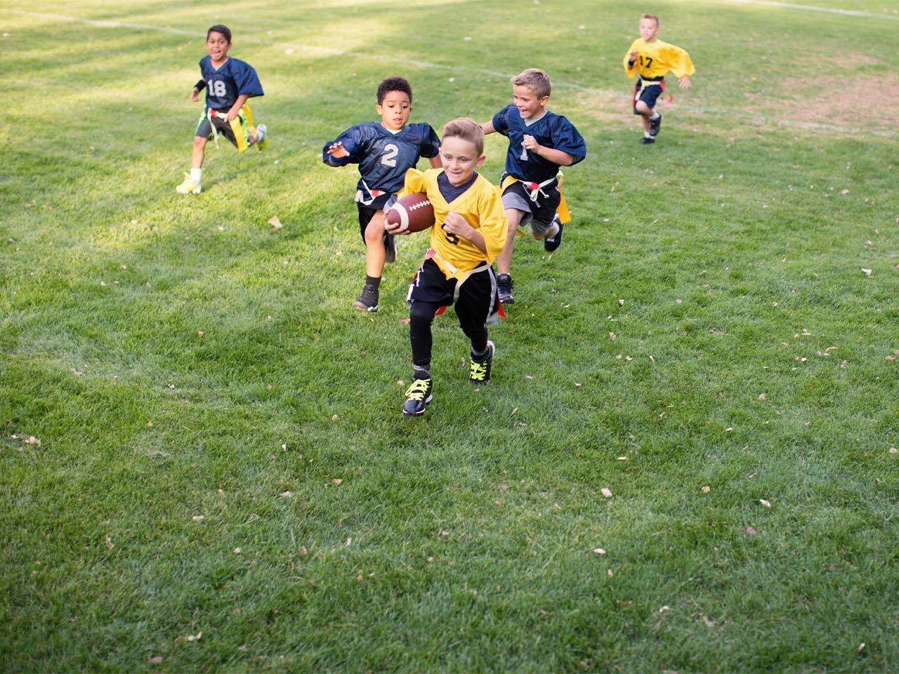 A group of children play flag football on a green field.