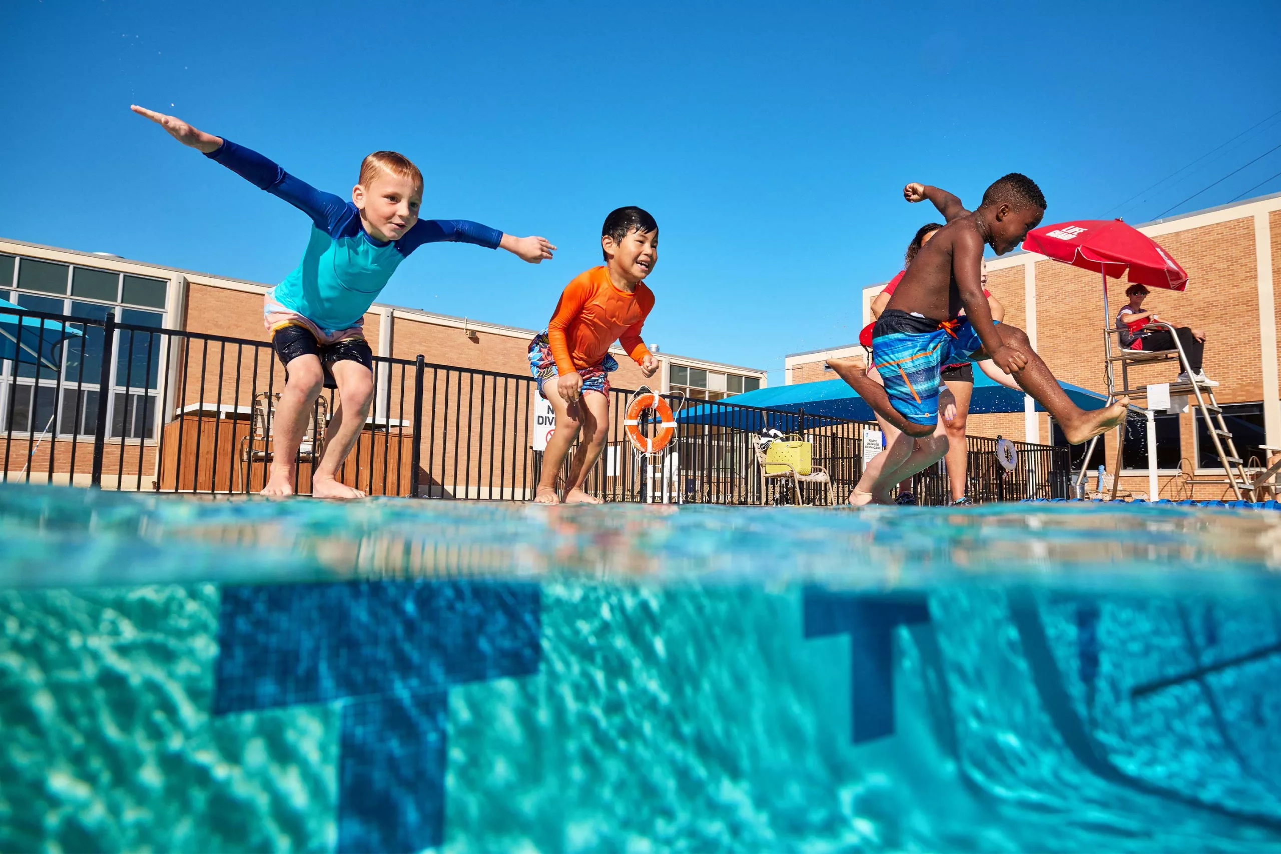 Children stand at the edge of the pool on the verge of jumping in. They are having fun.