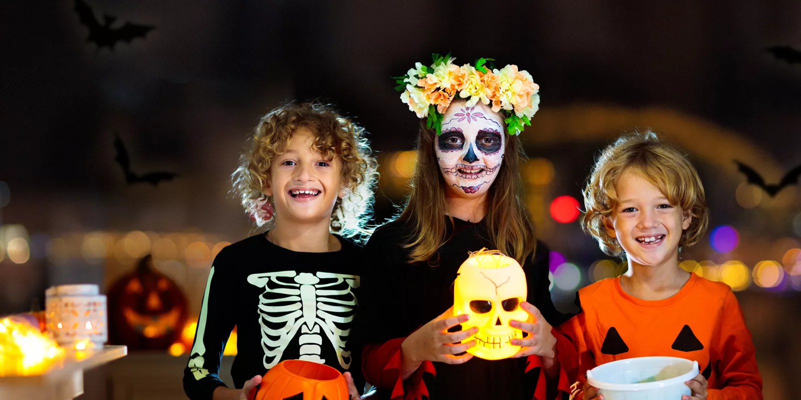 children wearing halloween costumes smile and hold spooky decorations