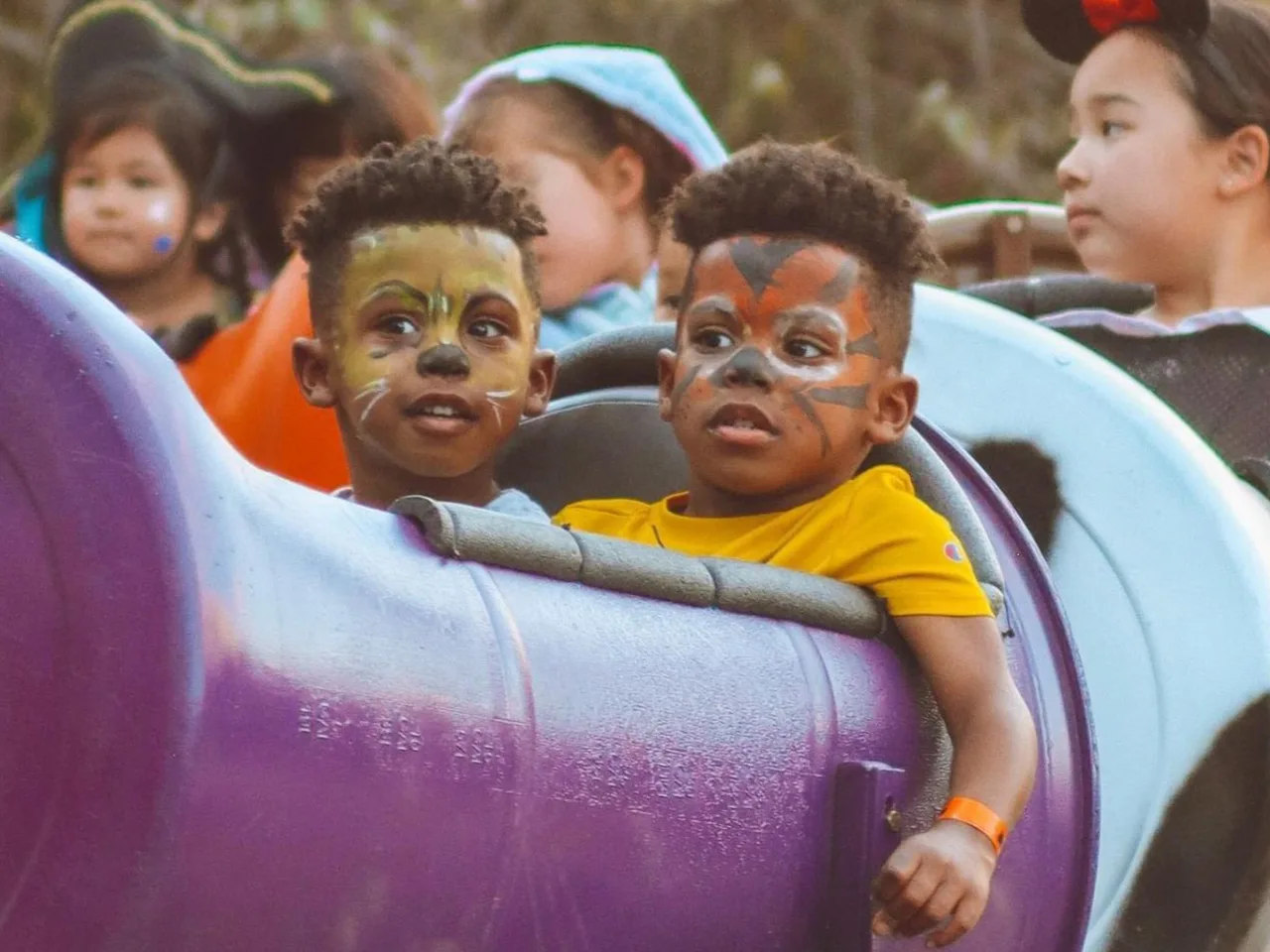 children with painted faces ride a fun train at a halloween party.