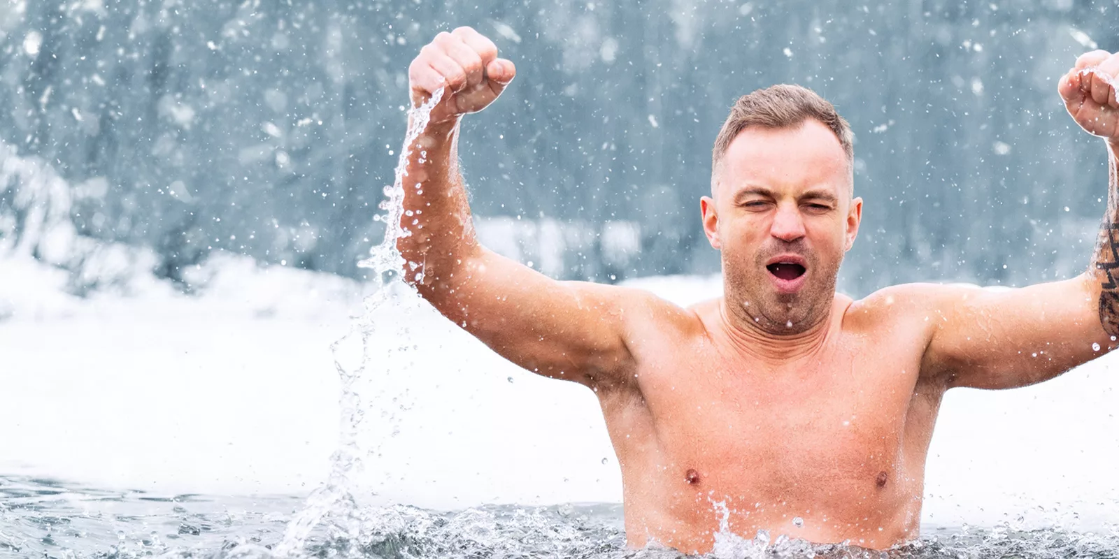 A man plunges into cold water and raises his arms as if in victory.