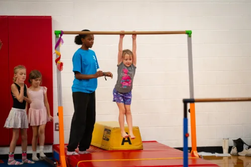 A child uses a gymnastics beam while an instructor provides guidance.