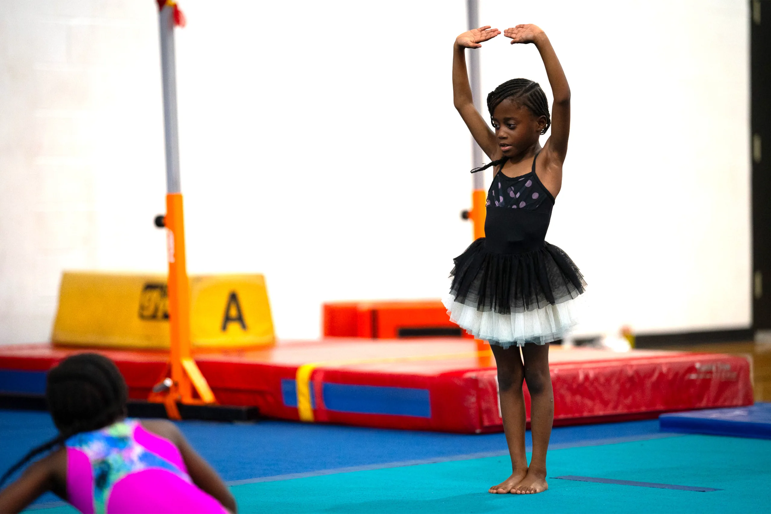 A child wearing a tutu holds her hands above her head.