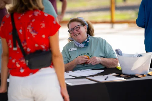 A woman smiles at a table outdoors.