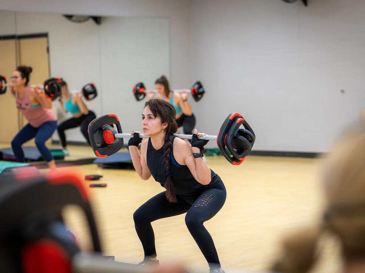 A woman squats in a group exercise class using a barbell.