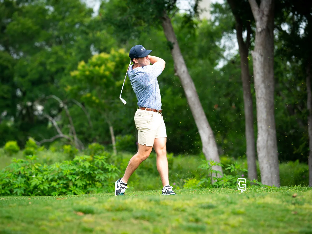 A man swings a golf club in a beautiful green golf course.