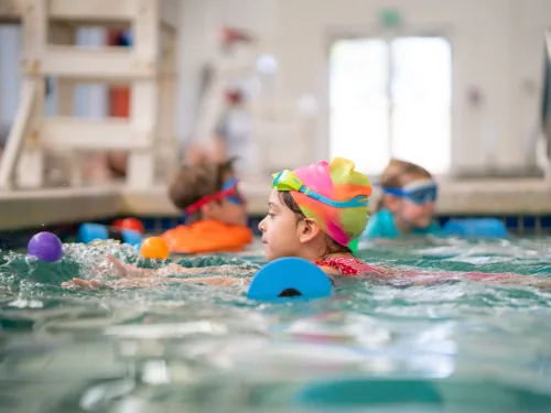 a child wearing a colorful swim cap participates in a swimming lesson in a pool.