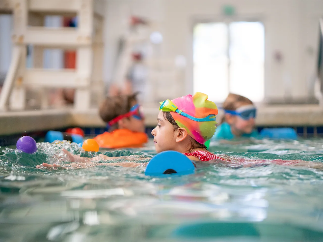 a child wearing a colorful swim cap participates in a swimming lesson in a pool.