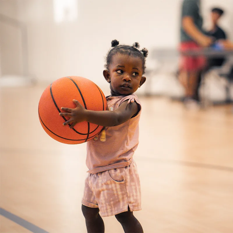 A toddler holds a basketball that is nearly as big as she is!