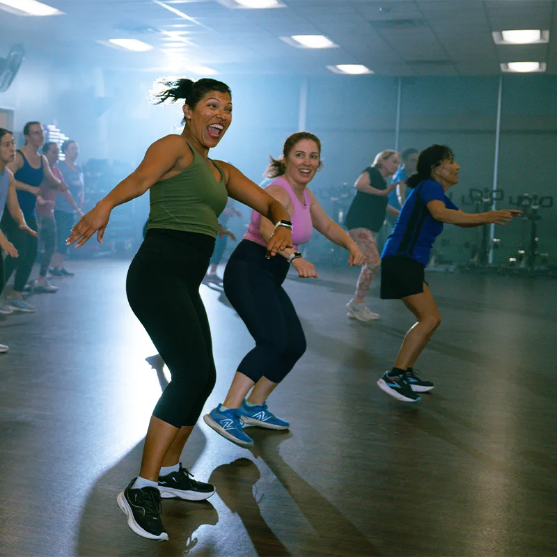 A group of adult women dance joyously in a Zumba class