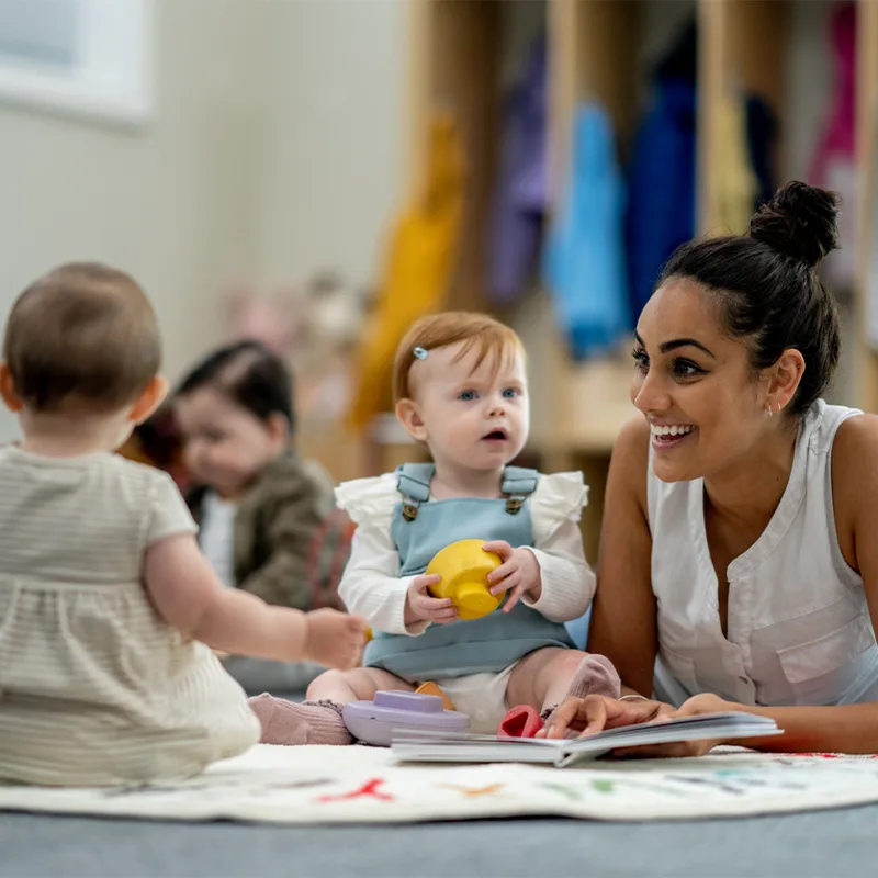 A woman lies on a floor playing with babies.