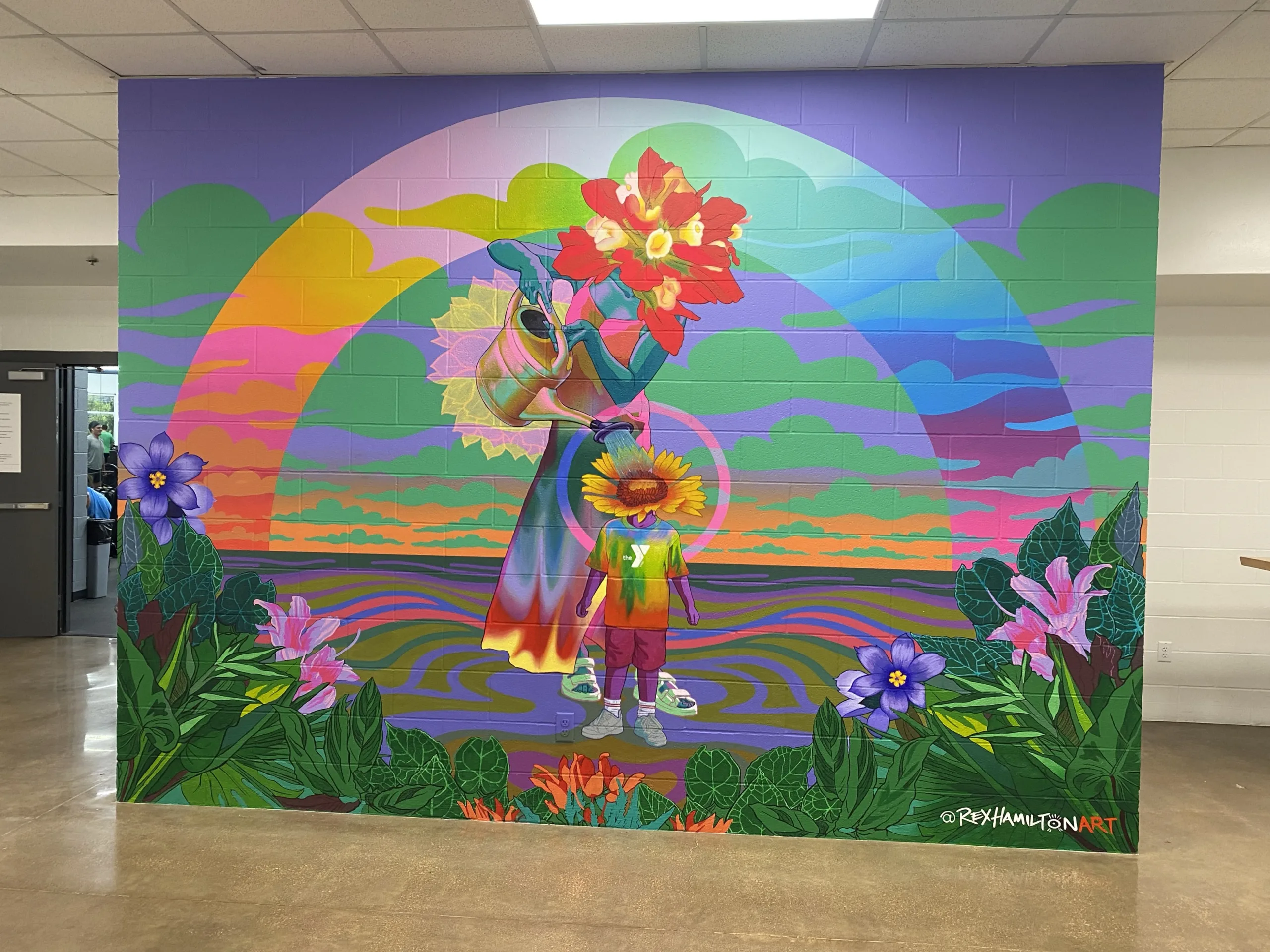 A colorful mural in the lobby at East Communities YMCA depicts a flower-grownup watering a flower-child.