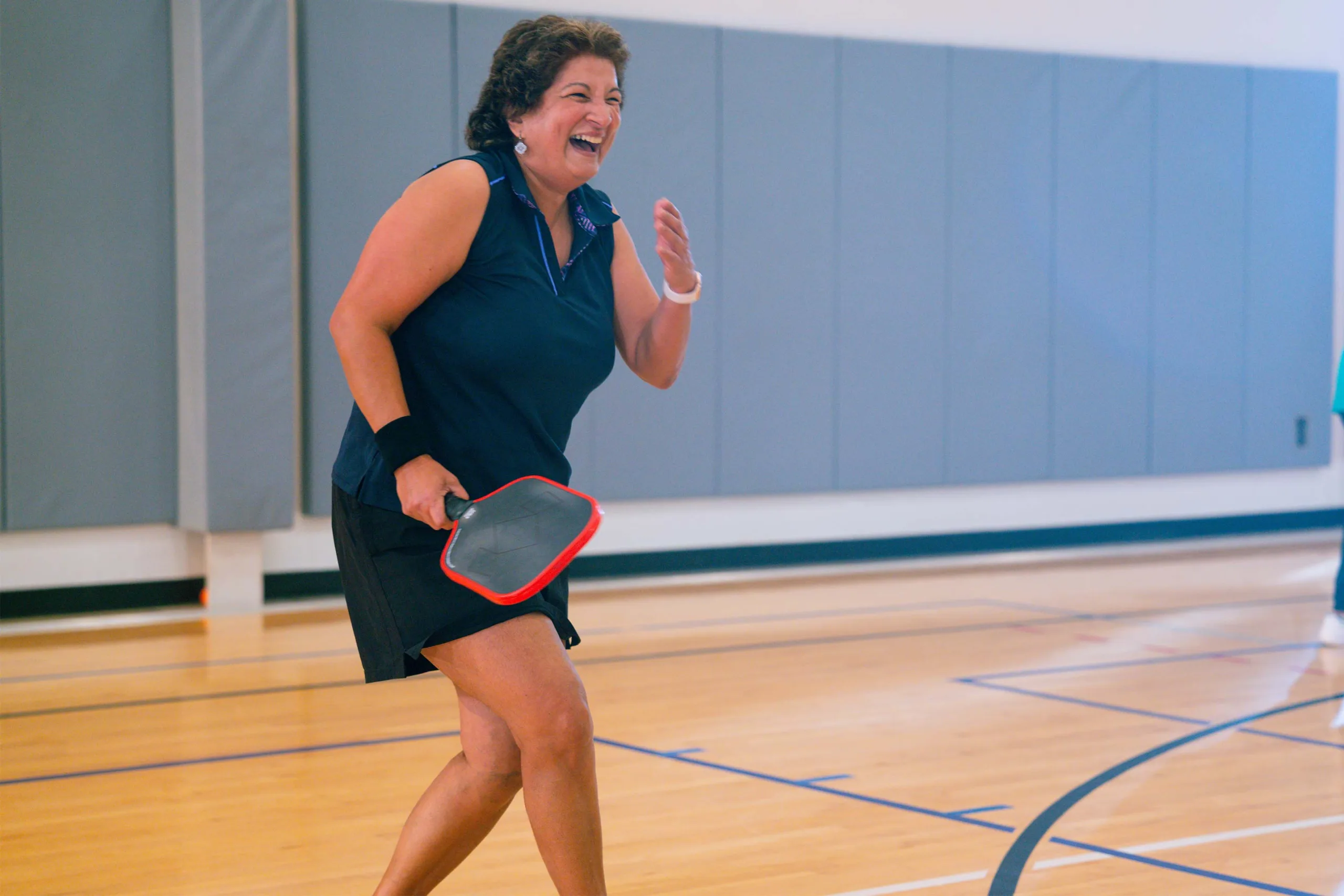 A woman smiles while playing indoor pickleball