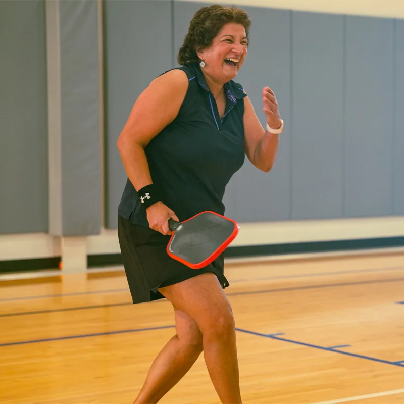 A woman smiles as she plays a game of indoor pickleball