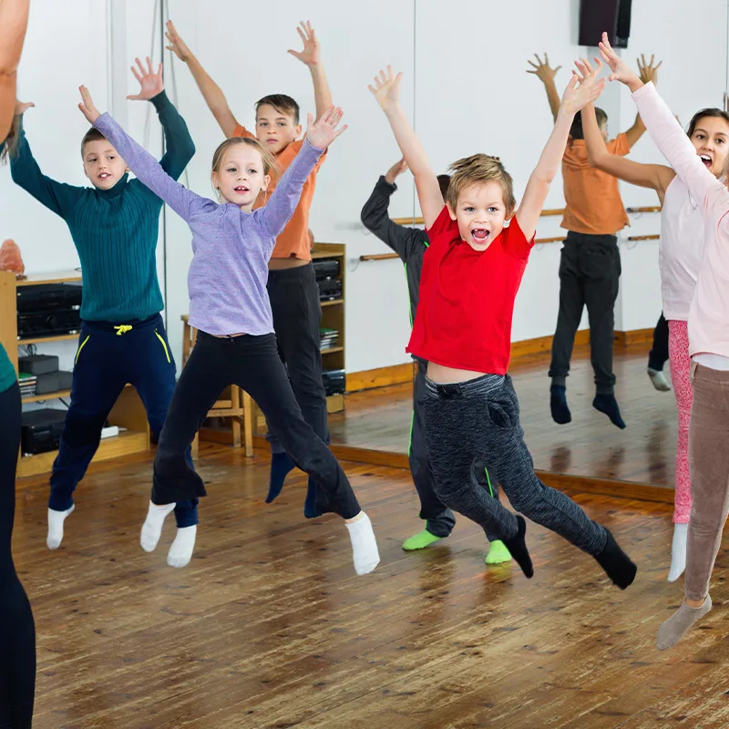 Children in a dance class jump with their hands in the air.