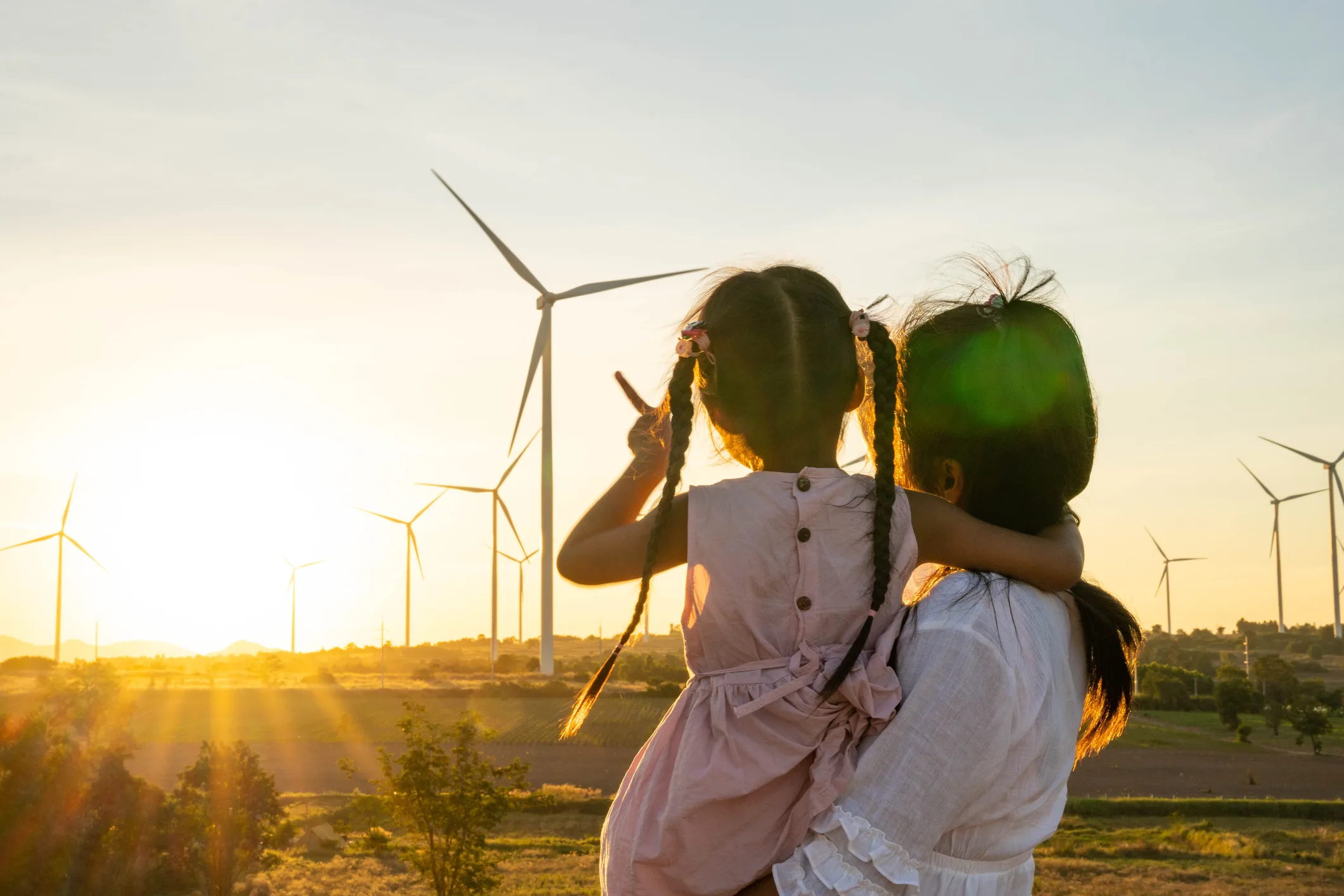 A mother holds her daughter while watching the sunset over a field of wind turbines