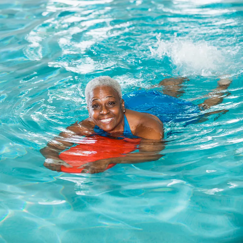 A woman smiles in a pool as she swims using a flotation device.