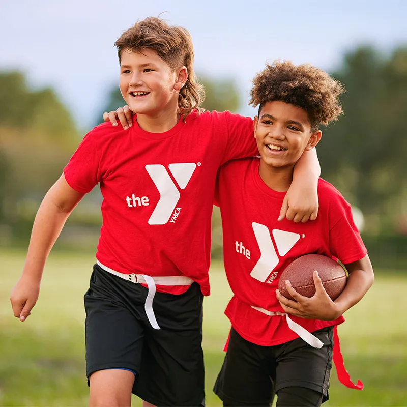 Two children smile with their arms around one another's shoulders. One child is holding a football.