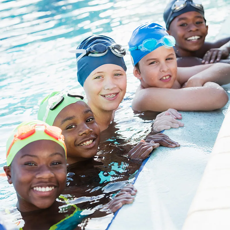 Children wearing colorful swim caps pose at the edge of a pool.