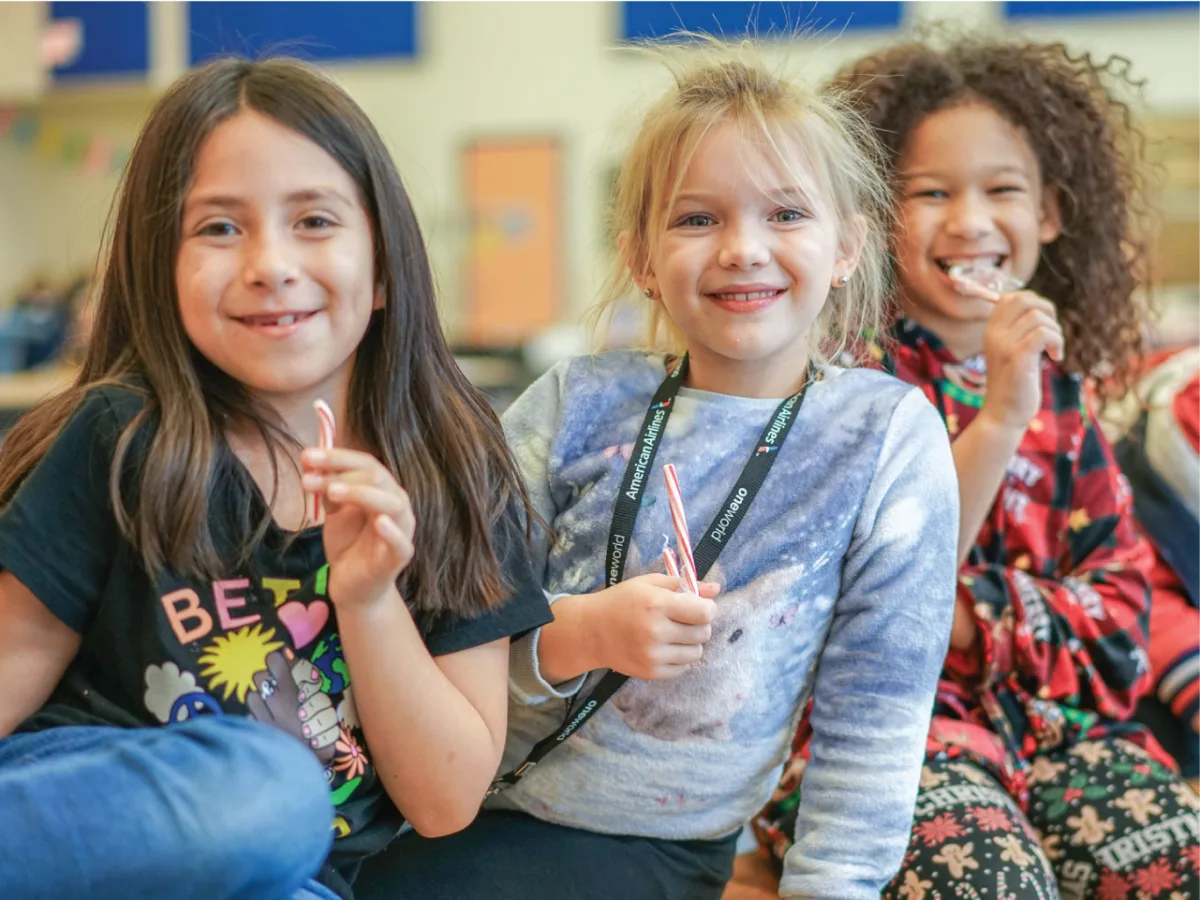 Three children sit together enjoying candy canes and smiling at the camera