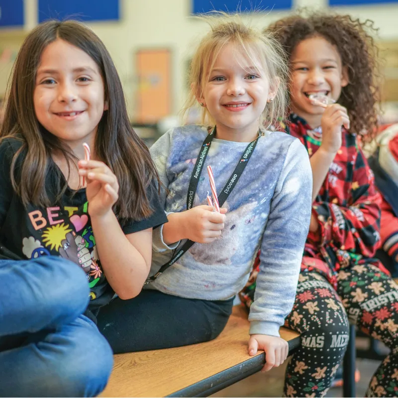 Three children sit together enjoying candy canes and smiling at the camera