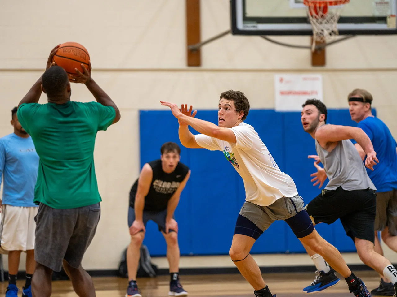 Adults play a game of basketball in an indoor gymnasium.