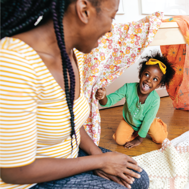 A parent and child play with a fort made out of sheets