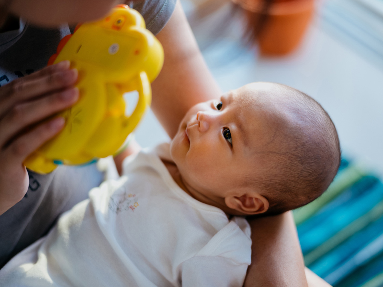 A person holds a baby and shows him a bright toy