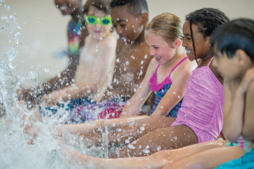 A group of children splash their feet in the pool with smiles.