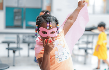 A girl enjoys a camp center where she gets to make believe that she's a superhero in pink mask and cape.