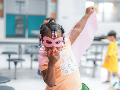 A girl enjoys a camp center where she gets to make believe that she's a superhero in pink mask and cape.