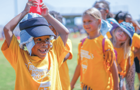 A child smiles broadly as they participate in a water cup relay game on Olympic Day.