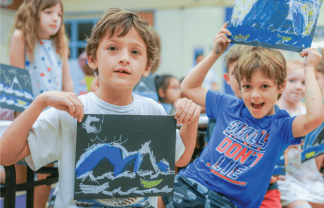 Children at camp show off their art projects where they made waves with chalk on black paper.