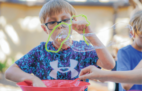 A boy blows big homemade soap bubbles through a pipe cleaner bubble wand.